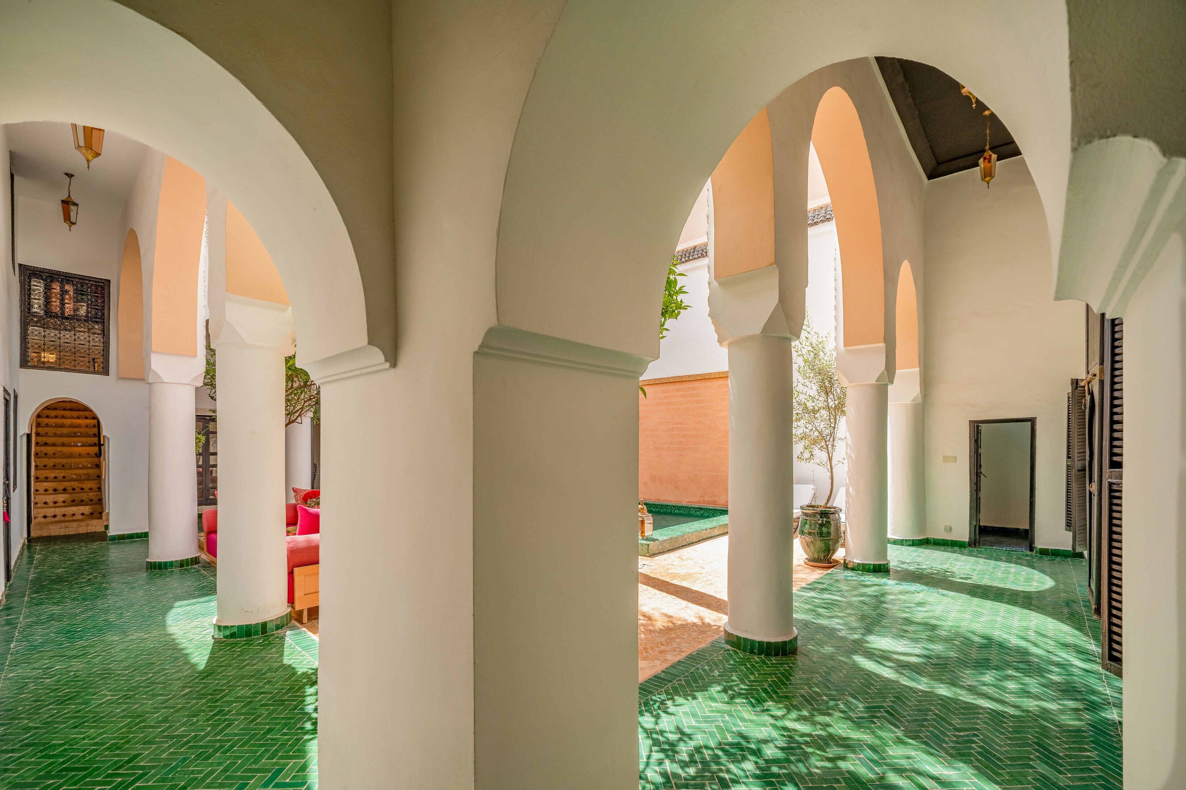 An interior corridor with arches, green tiled flooring, and a wooden door.