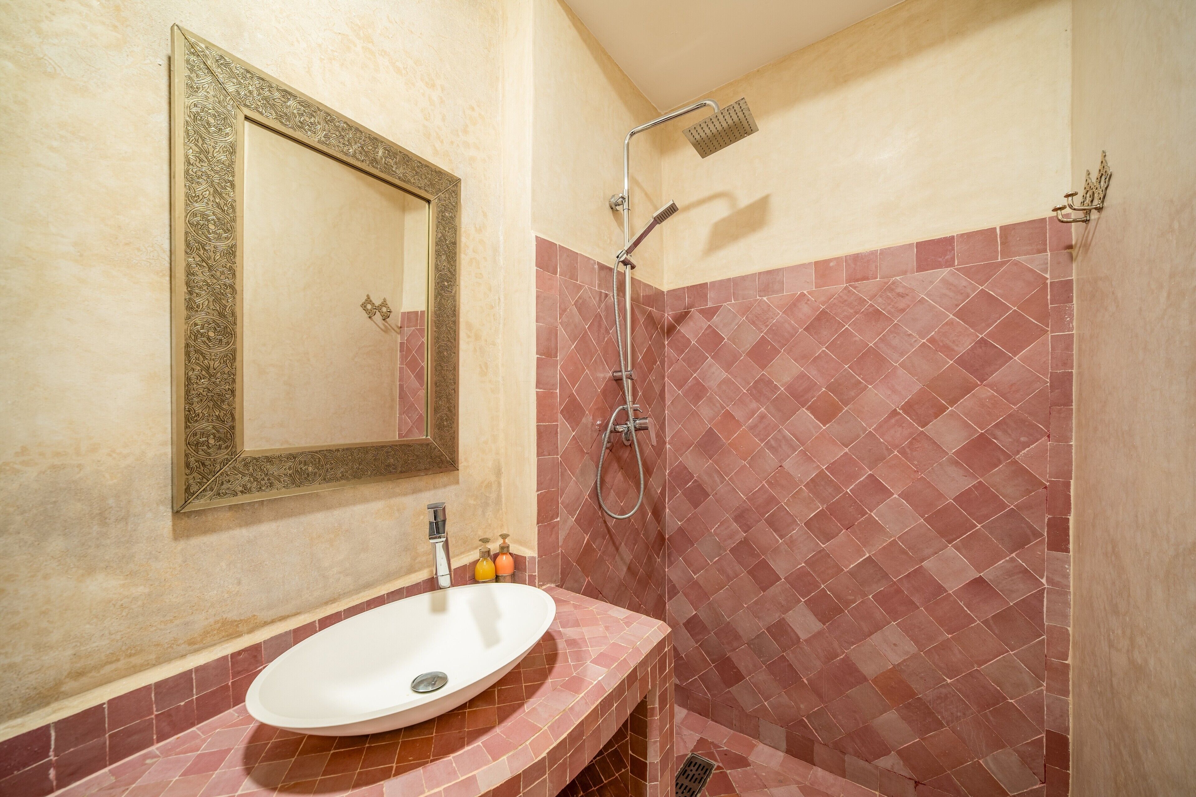 A bathroom with a white sink, a mirror with an ornate frame, and a shower area with red-tiled walls.