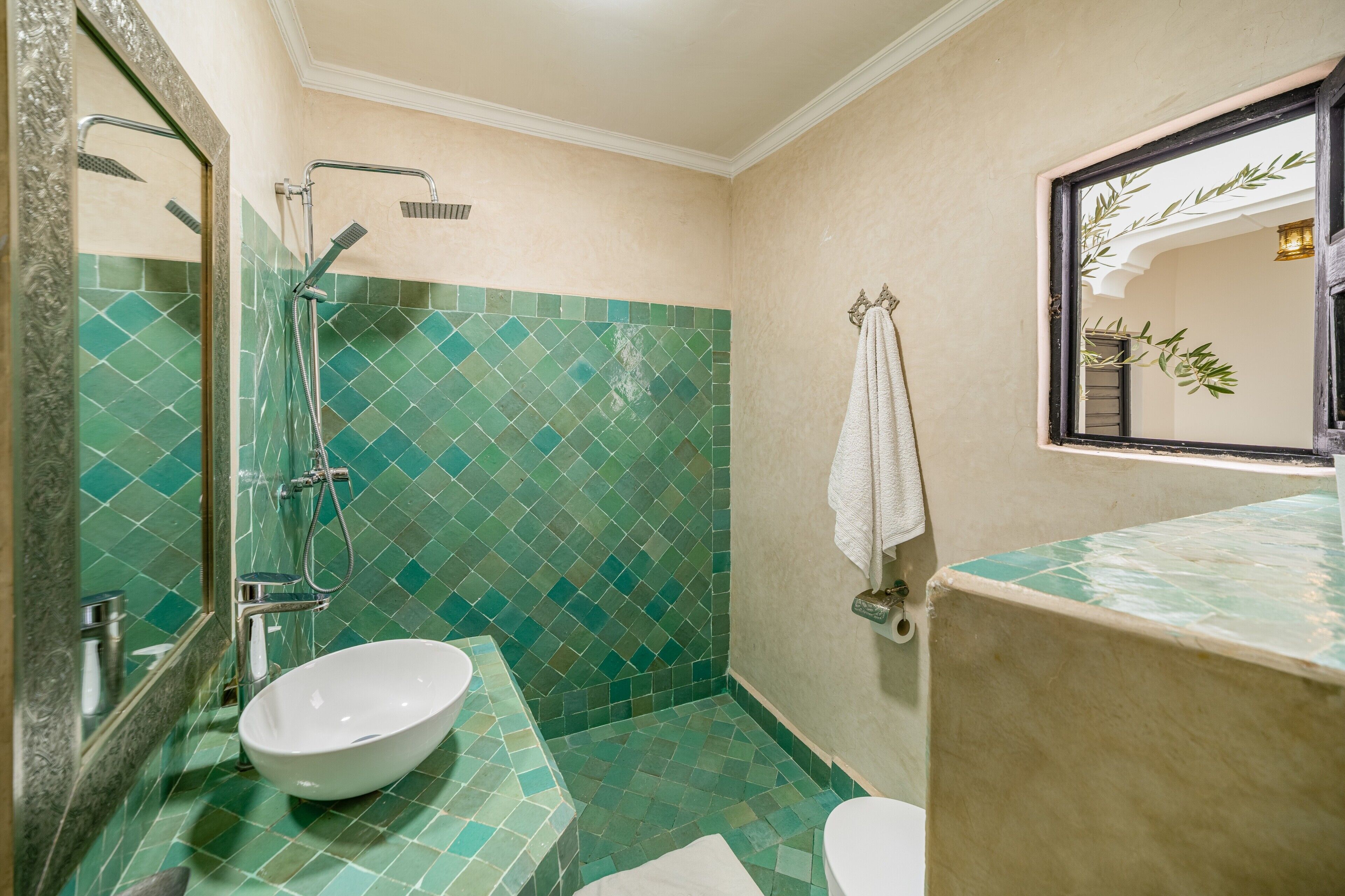 Een badkamer met een wit wastafelmeubel, een douche met glazen deur, en een muur betegeld met groene mozaïektegels.