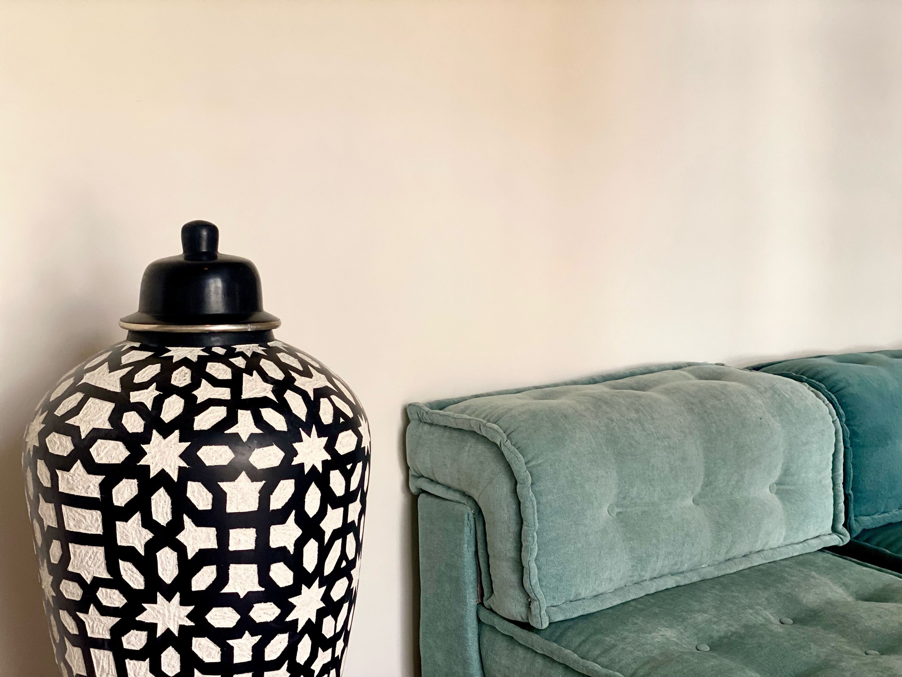 Een grote decoratieve vaas met een zwart-wit geometrisch patroon naast een smaragdgroene gestoffeerde bank.