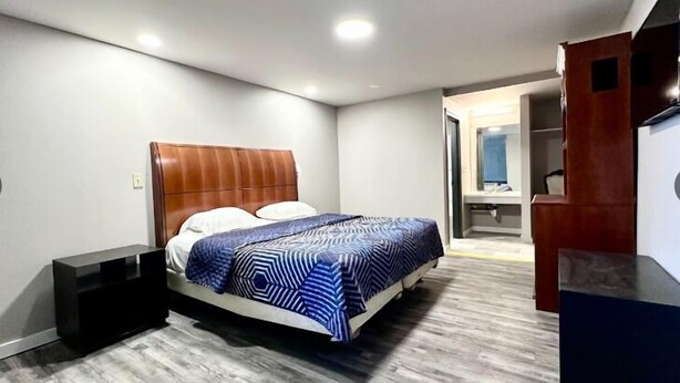 A modern bedroom with a wooden headboard, a patterned bedspread, and a built-in bench. - Three Judges Motel (New Haven)