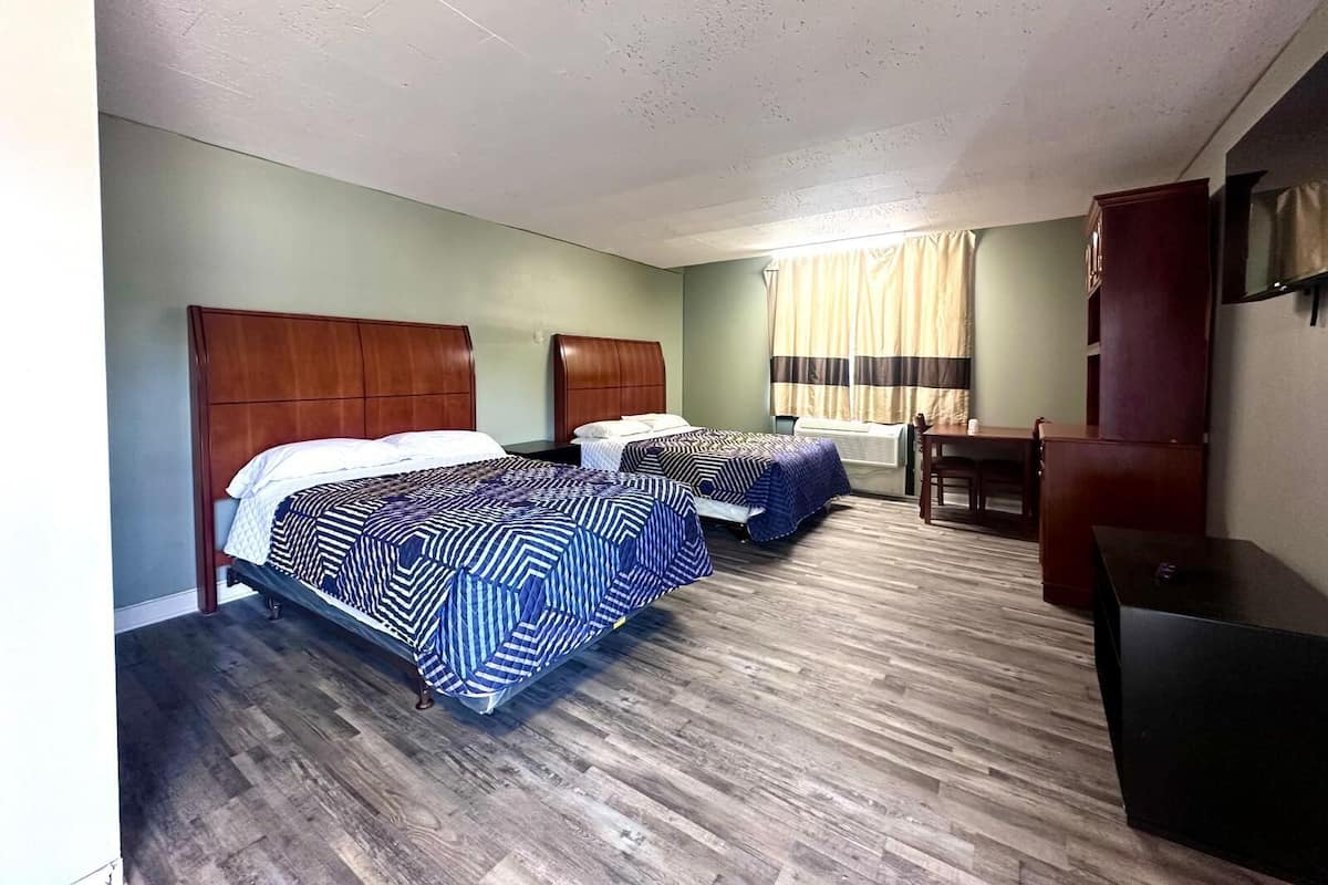A hotel room with two beds, a wooden floor, a desk, and a window with curtains.
