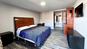A hotel room with a wooden headboard bed, a patterned bedspread, a small bedside table, a mirror, and a flat-screen TV. - Three Judges Motel (New Haven)