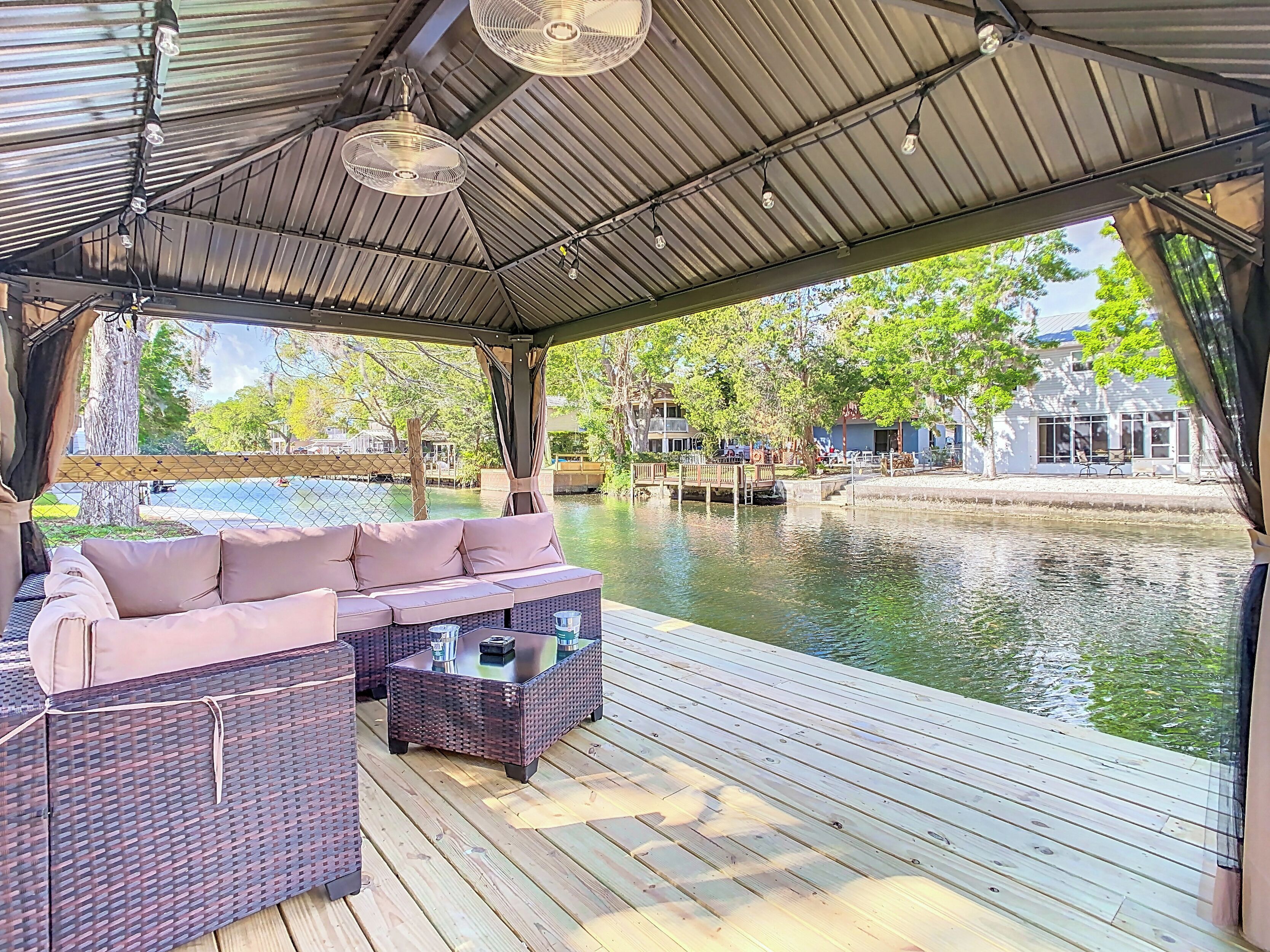 Een overdekt terras met rieten meubilair en uitzicht op een waterpartij.