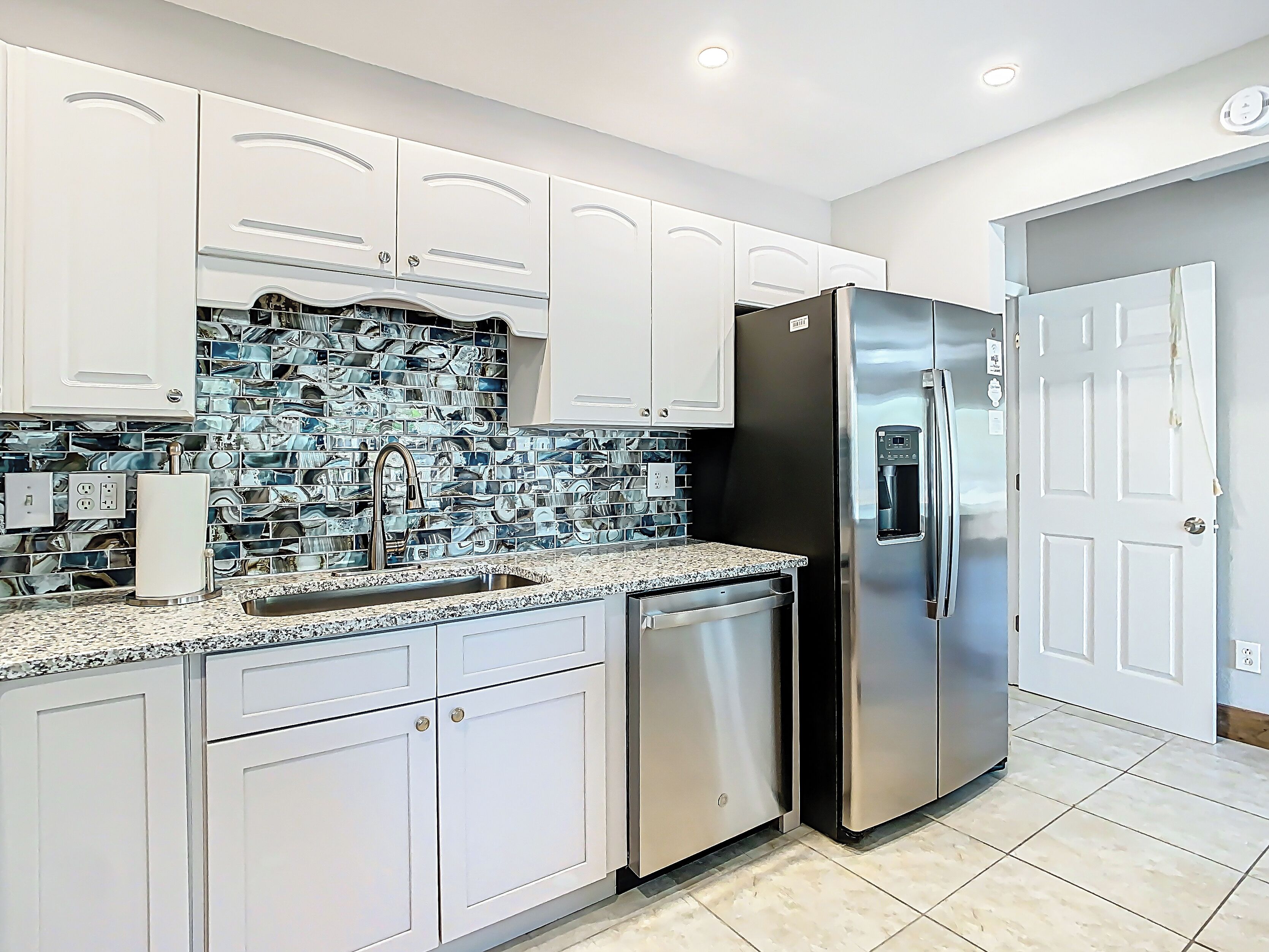 Una cocina moderna con armarios blancos, un refrigerador de acero inoxidable y un salpicadero de azulejos.
