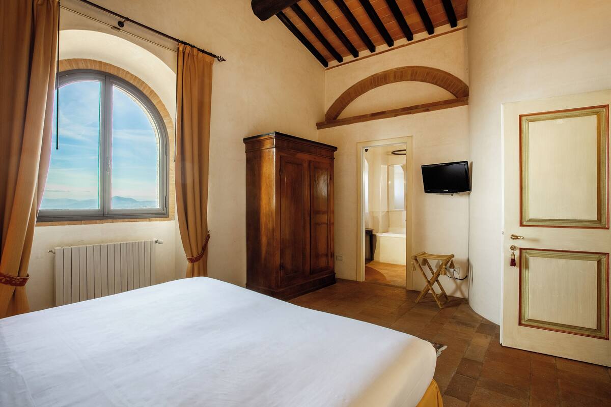A bedroom with a large bed, a wardrobe, a television, and a view through a window.