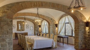Un espace repas avec une longue table dressée pour le repas, des arches en pierre et de grandes fenêtres.
