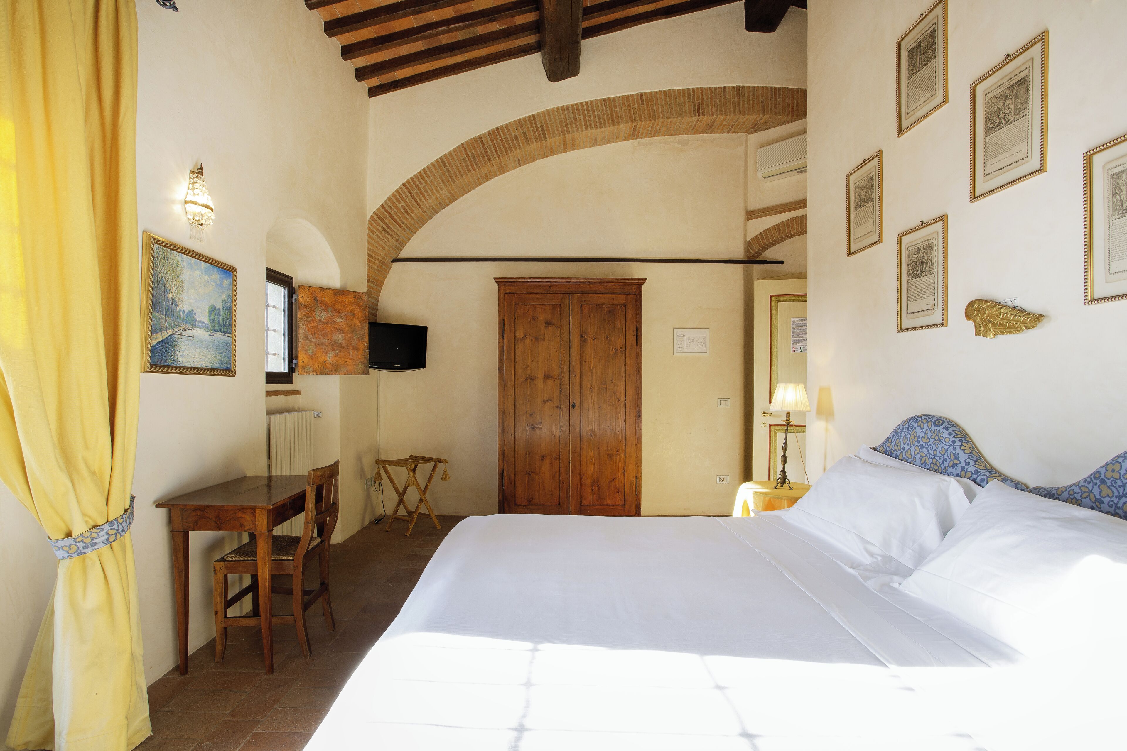 Un dormitorio con cama, un escritorio de madera, una silla, televisor y cuadros en la pared.