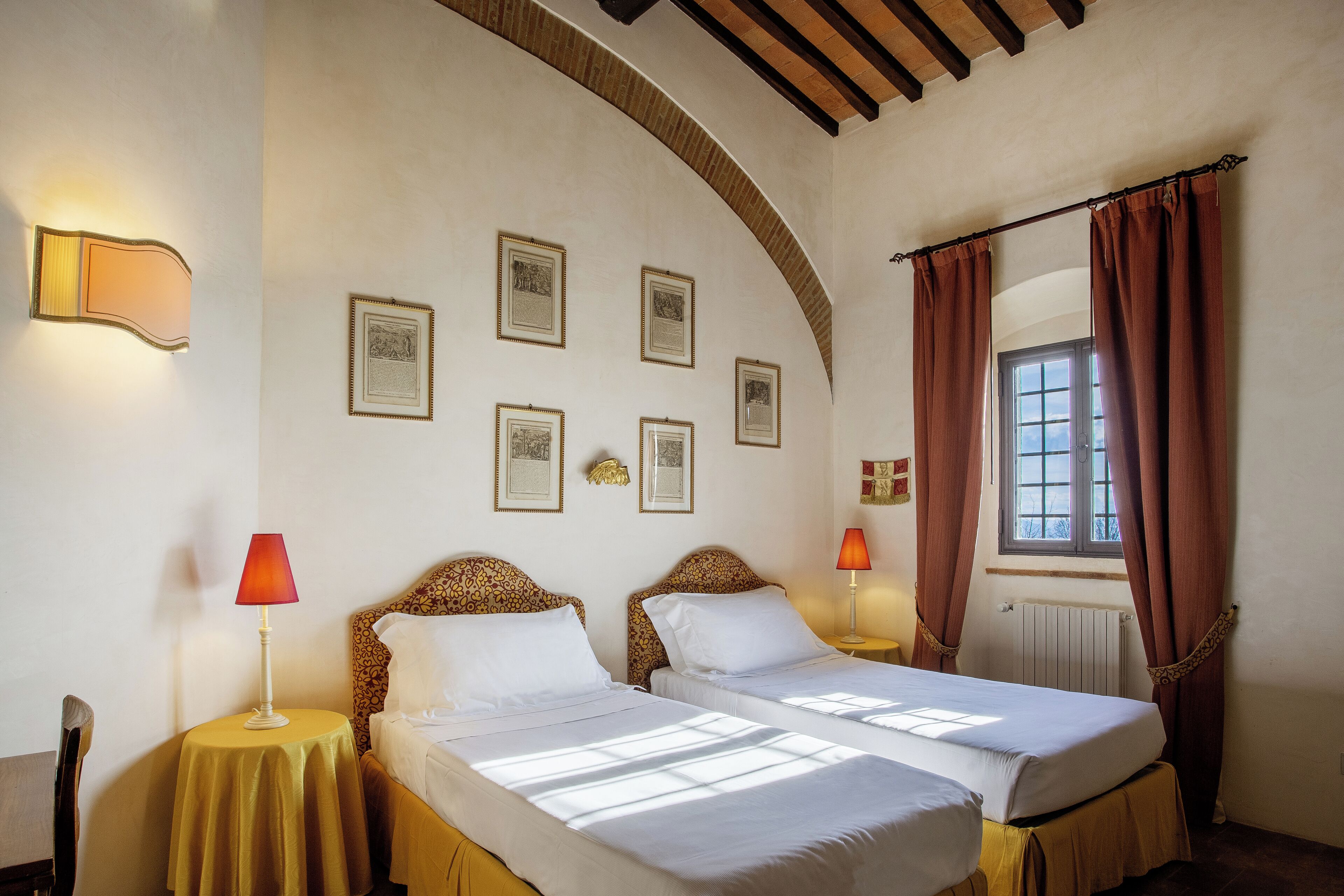 Habitación de hotel con dos camas, una mesa y un ventanal con cortinas.