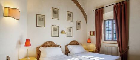 Habitación de hotel con dos camas, una mesa y un ventanal con cortinas.