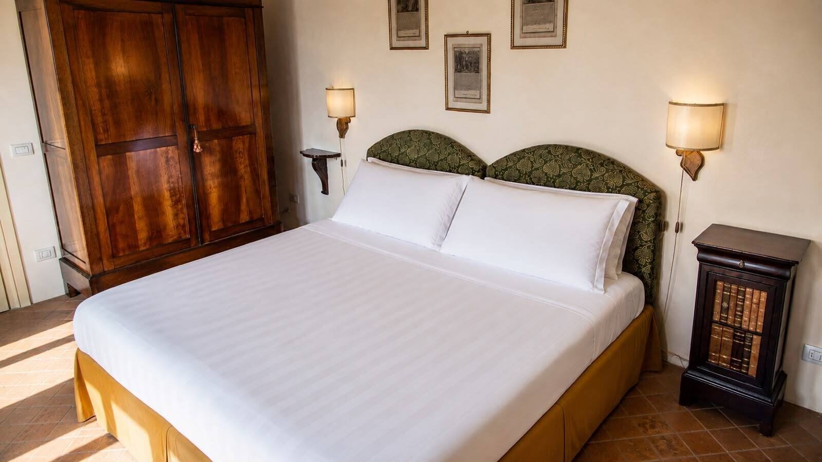 Een bed met een houten hoofdbord, twee bedlampen en een klein nachtkastje met boeken.