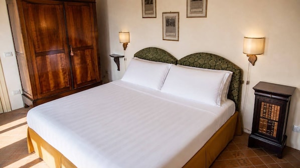 A bed with a wooden headboard, two bedside lamps, and a small bedside table with books. - Castello Di Montemasso (Greve in Chianti)