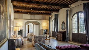 Une pièce spacieuse avec un haut plafond en bois, une cheminée et une grande porte en arc de cercle. On y trouve plusieurs meubles anciens, dont un canapé et des fauteuils.
