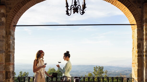 Une table dressée pour deux personnes, avec vue sur un paysage lointain, un lustre et une nappe.