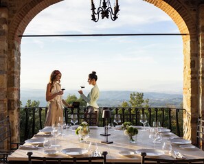 A table set for two with a view of a distant landscape, a chandelier, and a tablecloth. - Castello Di Montemasso (Greve in Chianti)