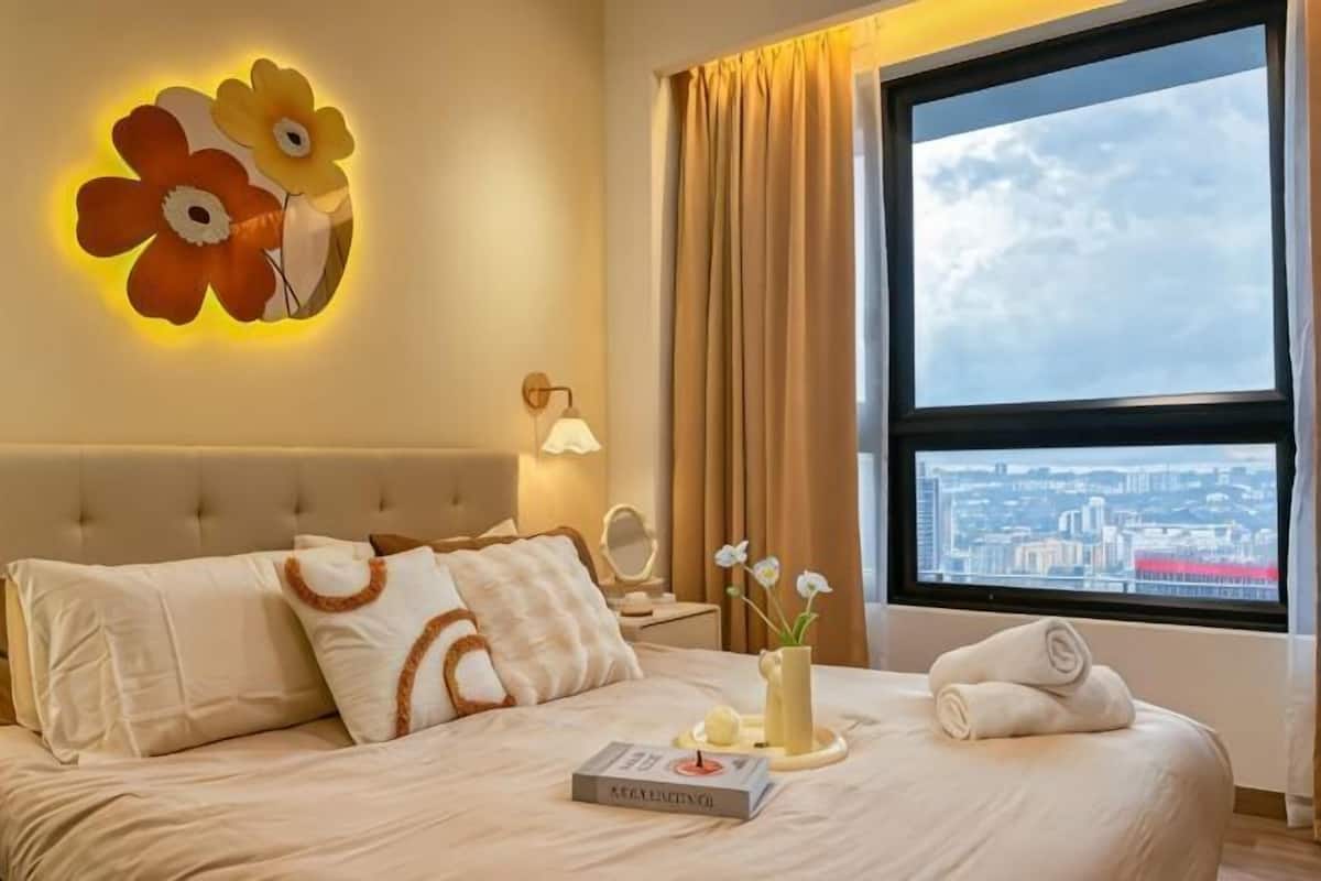 Une chambre d’hôtel avec un grand lit, une vue sur la ville, une décoration florale murale et une table de chevet avec une lampe.