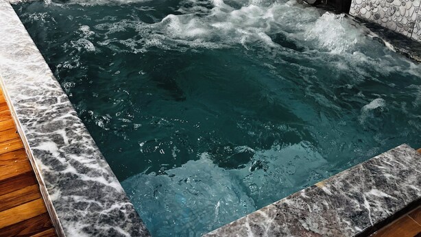 A hot tub with a marble border, surrounded by a wall with a pebble pattern. - Doğal Termal Suit (Gediz)