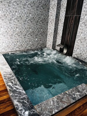 A hot tub with a marble border, surrounded by a wall with a pebble pattern.