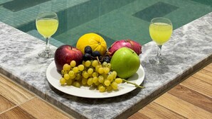 A poolside area with a marble table holding a plate of fruit and two glasses of a yellow beverage. - Doğal Termal Suit (Gediz)