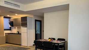 A modern living room with a sofa, dining table, and chairs. There is a kitchen area with cabinets and a refrigerator. - Doğal Termal Suit (Gediz)