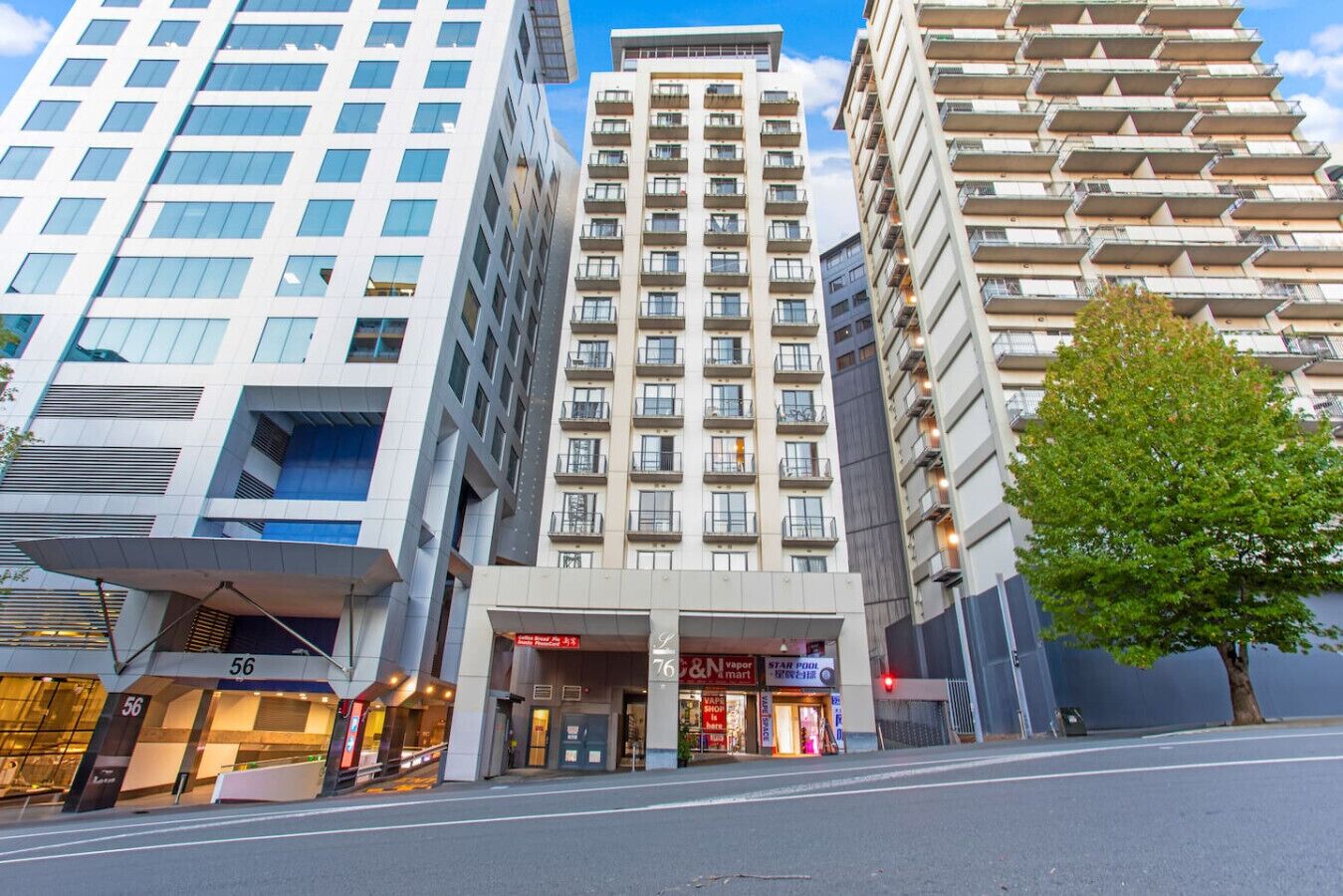 A modern hotel with a central entrance, multiple floors, and a large tree in front.