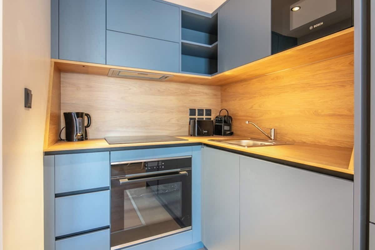 Une cuisine compacte avec des meubles bleus, un plan de travail en bois, un four encastré et un lave-vaisselle Bosch.