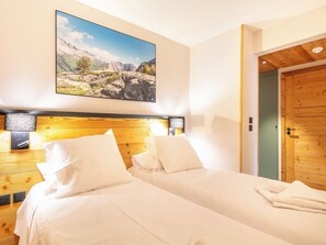 A hotel room with two beds, a wooden headboard, a large landscape painting, and a wooden door. - Les Hauts de Vaujany - Vacancéole (Vaujany)