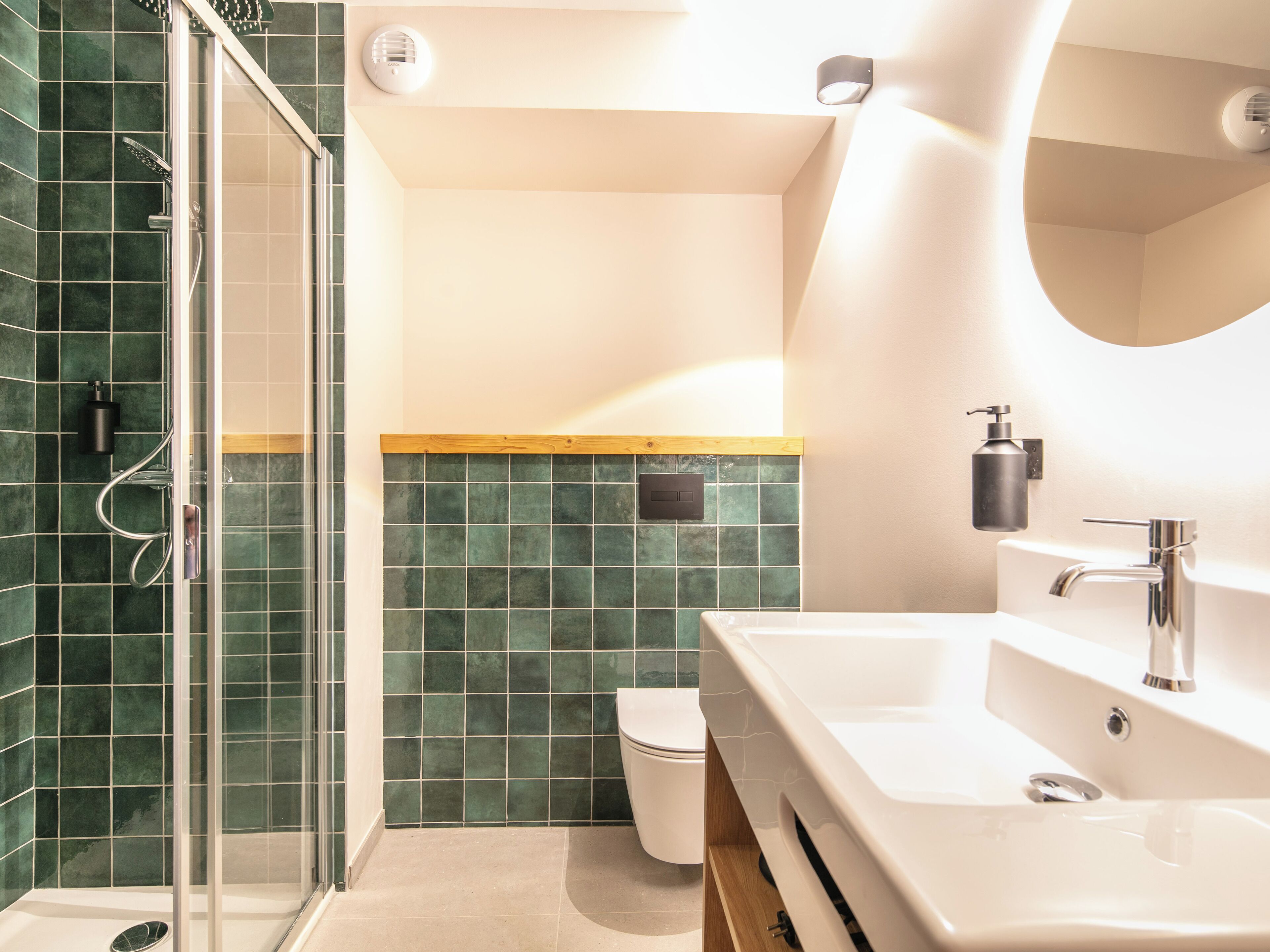 A modern bathroom with a glass shower enclosure, a white sink with a soap dispenser, and a toilet.
