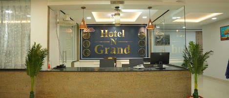 A hotel reception desk with a sign reading "Hotel N Grand" and a reception area with two potted plants.