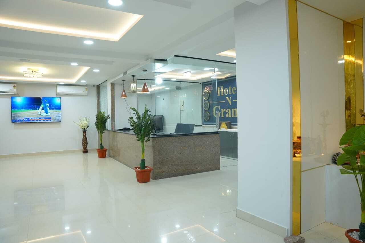 A hotel reception area with a modern design, featuring a reception desk, a television mounted on the wall, and potted plants.