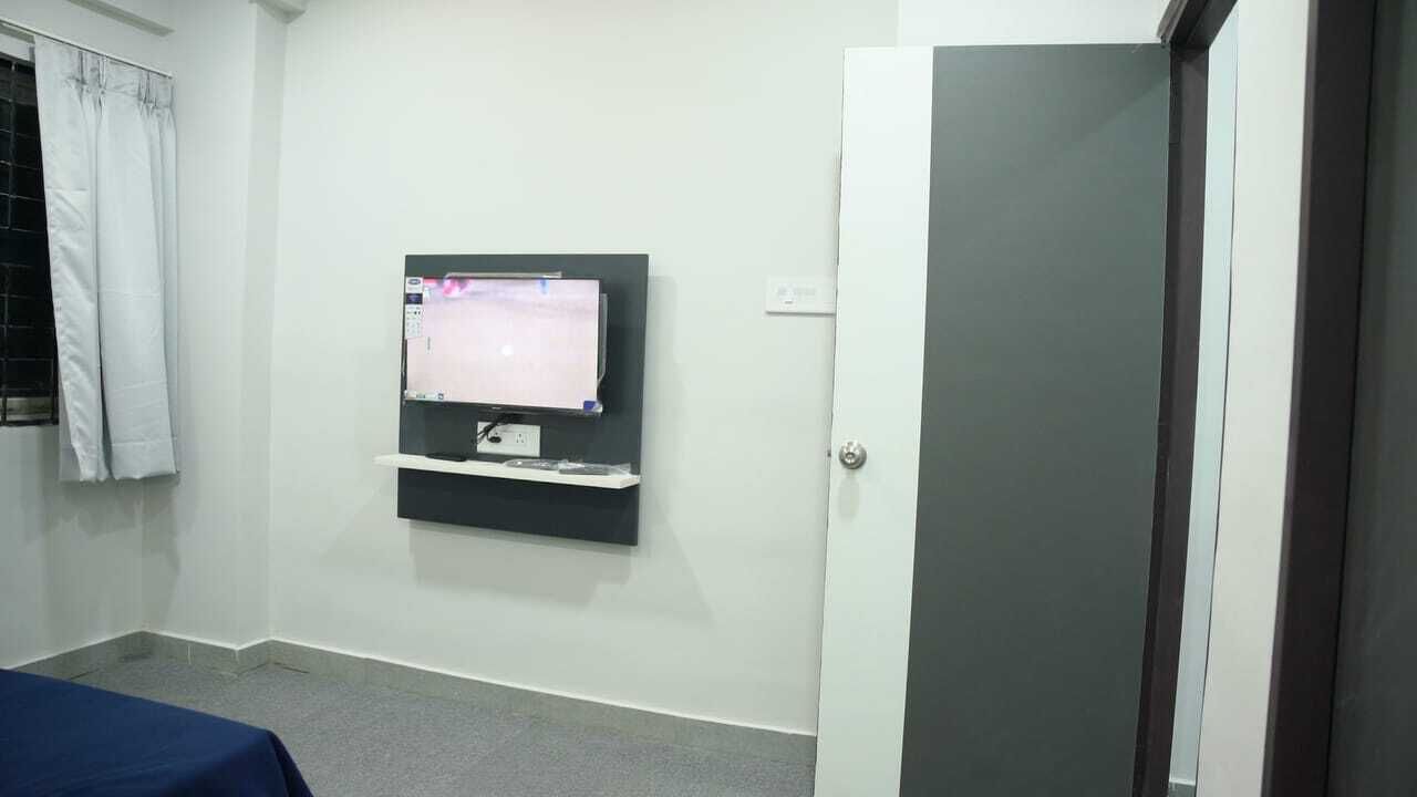 A room with a bed, a TV mounted on the wall, a door, and a window with curtains.