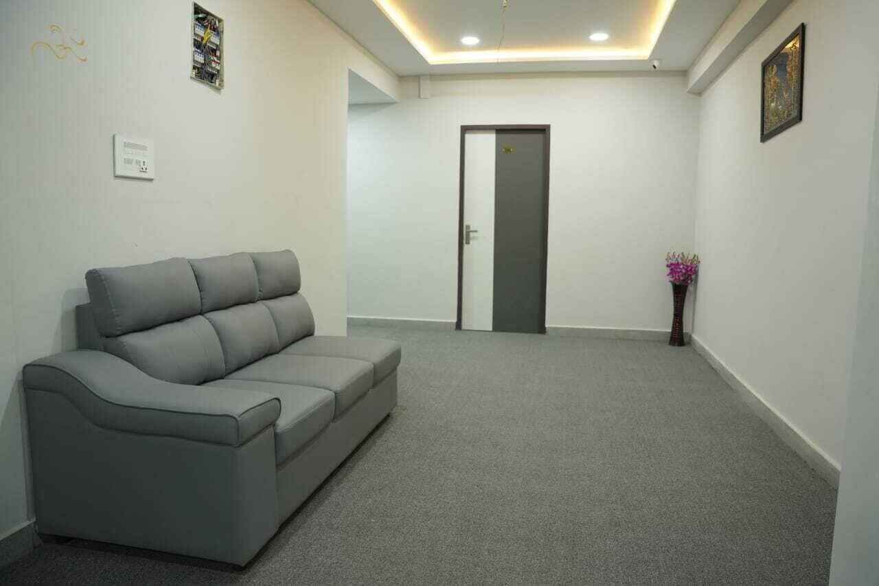 A neutral-colored room with a grey sofa, a door, and a small vase with flowers.