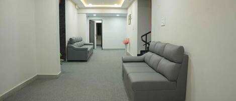A modern living room with a grey sofa, a smaller grey armchair, and a coffee table. The room has a neutral color palette and a carpeted floor.
