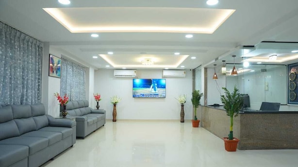 Un área de recepción moderna con un sofá, plantas en macetas, un televisor y un mostrador de recepción.