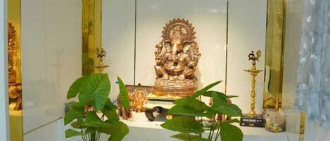 A room with a central statue, two potted plants, and a small table with a decorative bowl.
