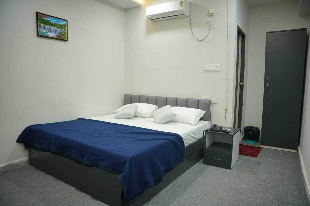A bedroom with a bed, a bedside table, a nightstand, an air conditioner, a door, and a wall-mounted picture.