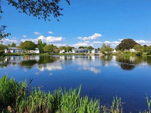Un lago tranquilo que refleja el cielo y árboles circundantes, rodeado de edificios y follaje.