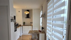 A modern kitchen with a dining area, wooden flooring, and large windows with blinds.