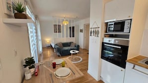 A compact living space with a kitchenette, a dining area with a table set for two, a sofa, and a hanging light fixture.