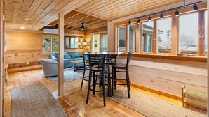 A wooden interior with a dining table and chairs, a sofa, and a large window. - Quarry Village Compound; 4BR + Hot Tub on a workin (Spruce Head)