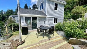 A house with a deck, a grill, and a patio table with chairs.