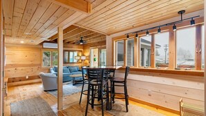 A wooden interior with a dining area, sofa, and large windows. - Pirate's Den on the Wharf (Spruce Head)