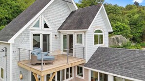 A two-story house with a balcony, large windows, and a wooden deck. - Pirate's Den on the Wharf (Spruce Head)