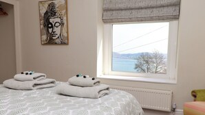 Un dormitorio con cama, ventana con vistas, un cuadro en la pared y una silla.