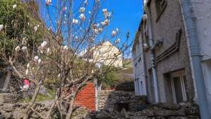 Un edificio con pared de piedra y puerta roja, rodeado de árboles con flores florecientes.
