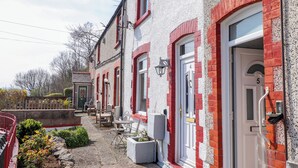 Fila de casas de ladrillo rojo y paredes blancas, con los números 4 y 5, con asientos exteriores y una pequeña zona de jardín.