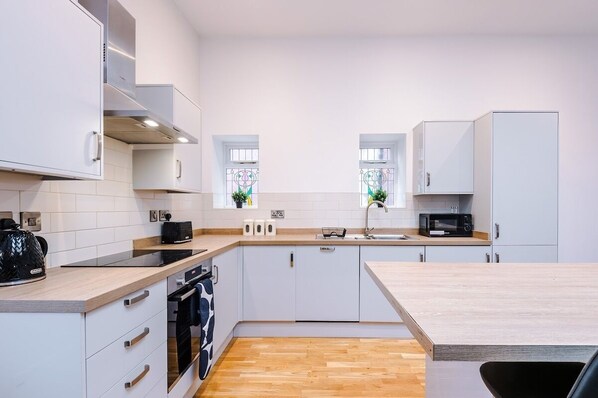 A modern kitchen with white cabinets, a wooden countertop, a built-in oven, a microwave, and a sink.