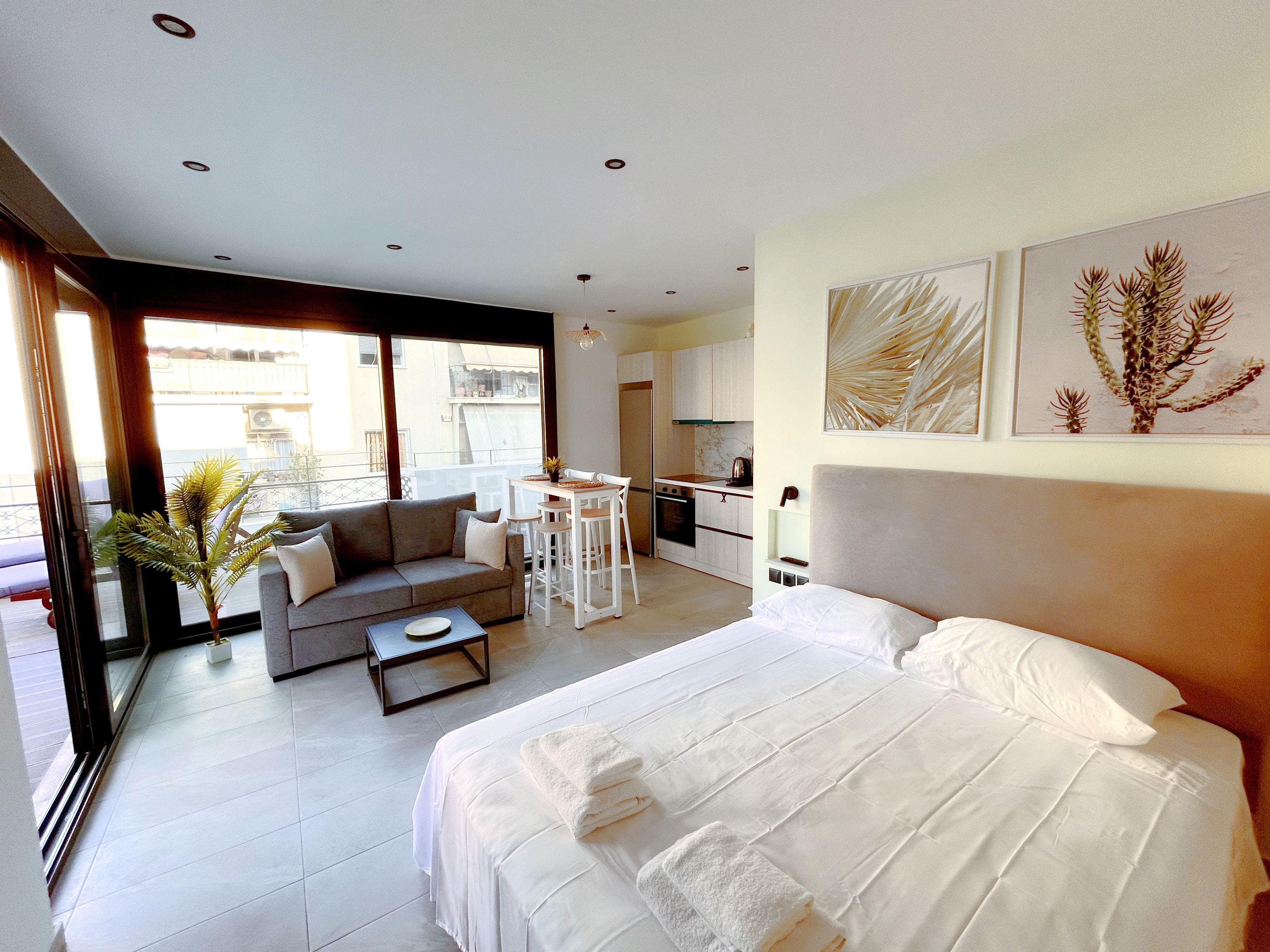 A modern hotel room with a large bed, a sofa, a dining table, and a kitchen area.