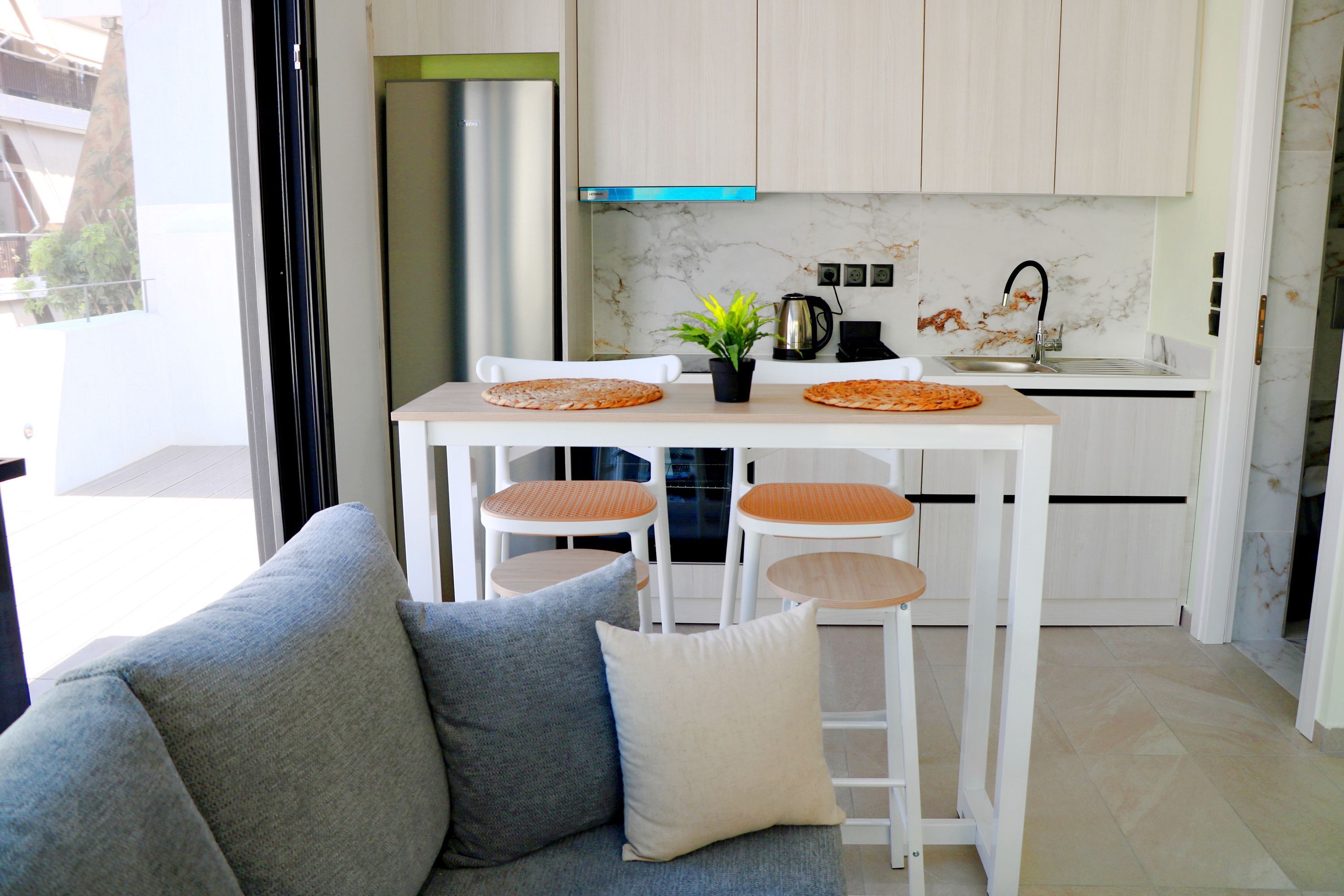 A modern kitchen with white cabinets, a marble backsplash, and a dining area with a sofa and chairs.
