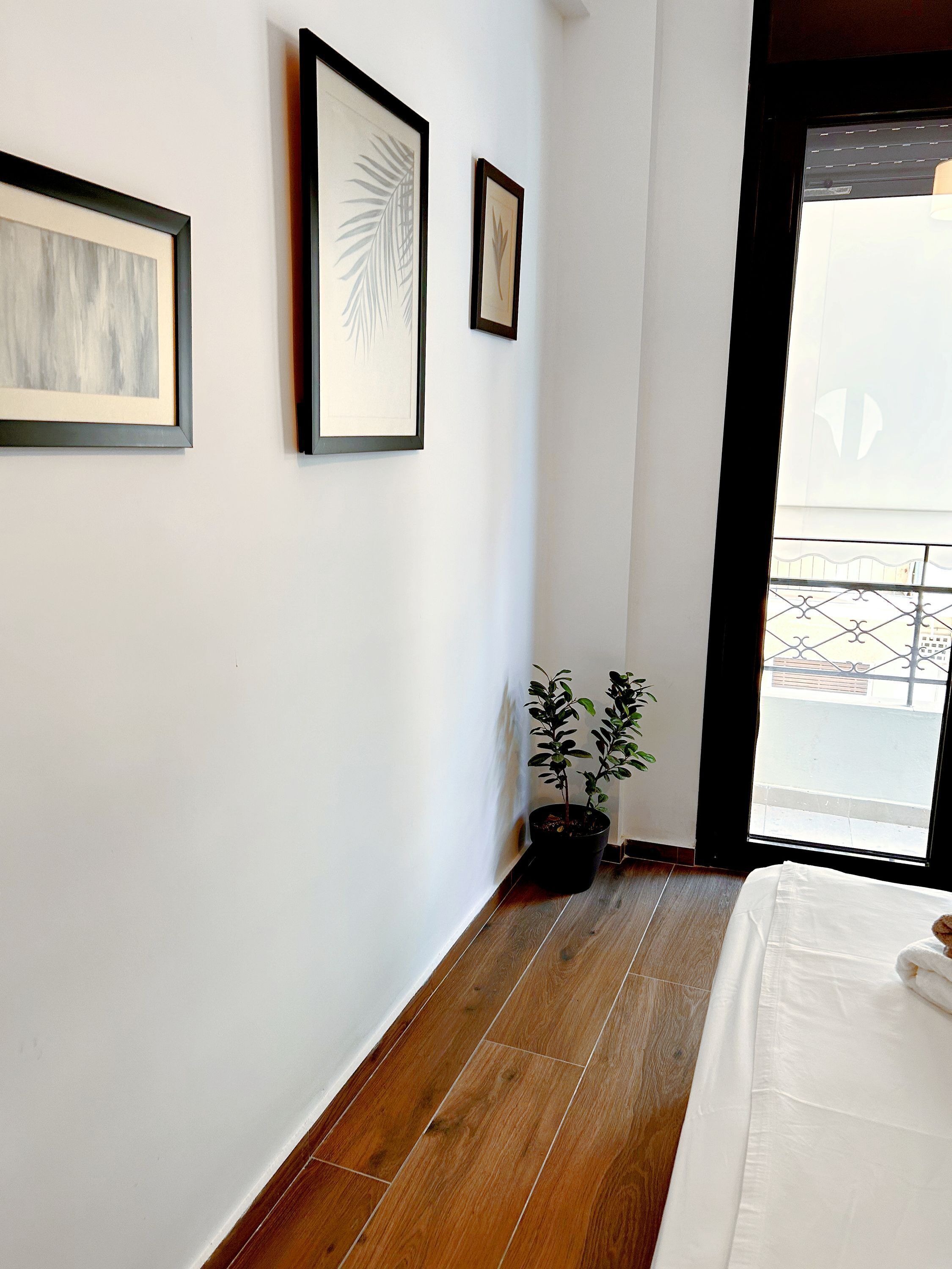 Ein Schlafzimmer mit Holzboden, einem Bett mit weißer Bettwäsche, einem Blumentopf und gerahmten Bildern an der Wand.